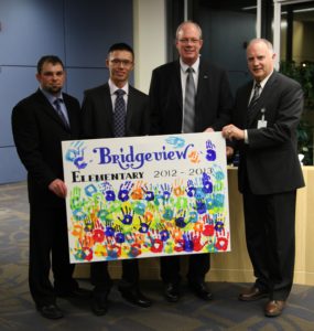 Bridgeview elementary school principal Andrew Shook (from left), Mainroad's Calvin Chan and Doug Bjornson and Surrey Board of Education chairperson Shawn Wilson with a thank-you poster from the students who, thanks to Mainroad, took swimming lessons this year. Every student who attended lessons âsignedâ the poster with their handprints.