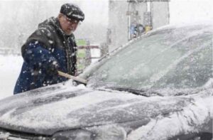 man scraping snow from windshield